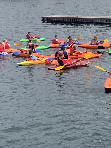 Children paddling a group of orange and green canoes